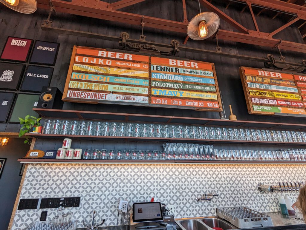 A view at the menu at Notch, with a long row of beer glasses on two shelves underneath.