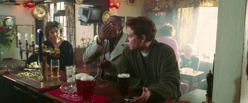 Ford Prefect stuffing his face with peanuts, while Arthur Dent hasn't even started his first. The beers sat on the bar for them are amber resp. dark amber.