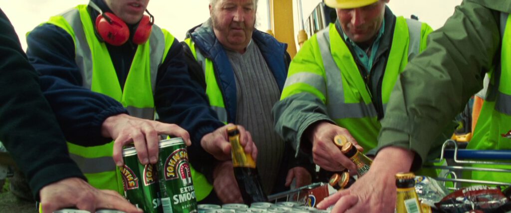 Construction workers in hi-viz picking cans of John Smith Extra Smooth and bottles of Cobra from a shopping trolley.