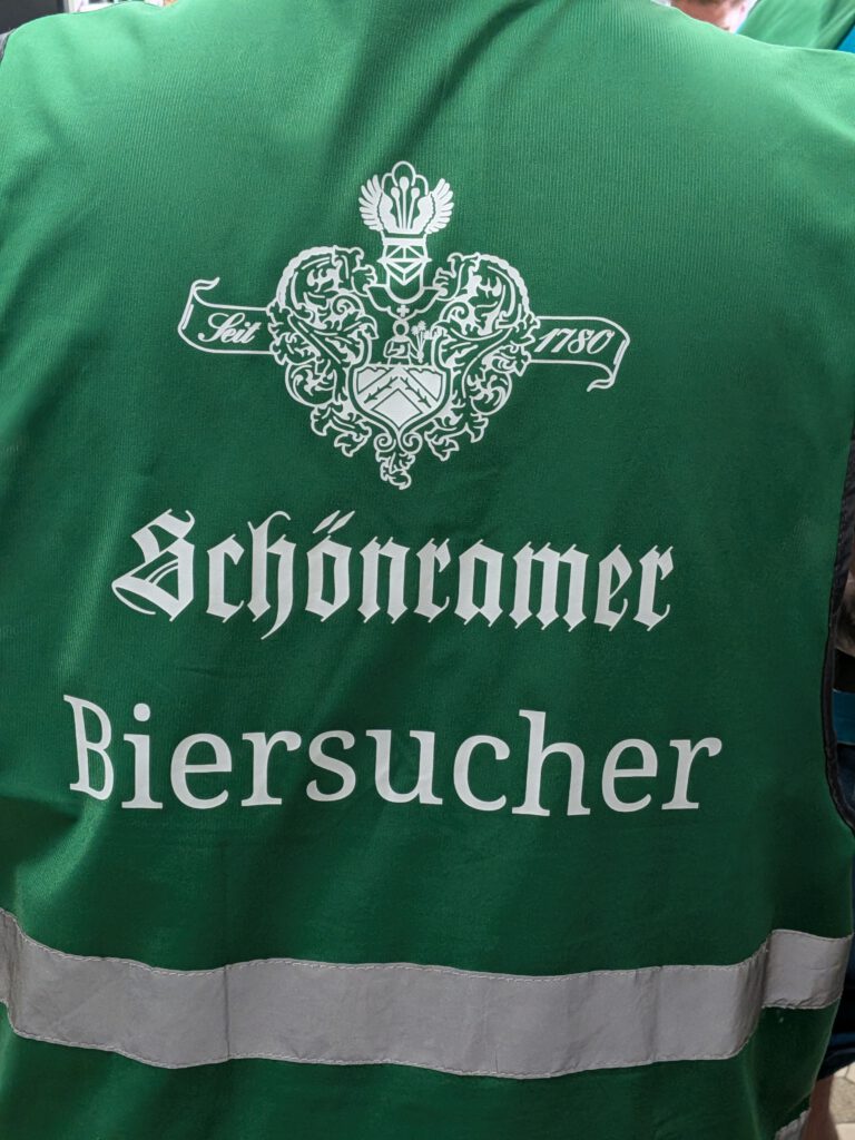 The back of a Schönramer-branded high-vis vest worn by a brewery tour participant. It says "Biersucher" on the back, a portmanteau of "Bier" and "Besucher" (visitor).