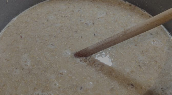 A mash, with noticeable husks and crushed grains in it, and a wooden mash paddle stuck in it.